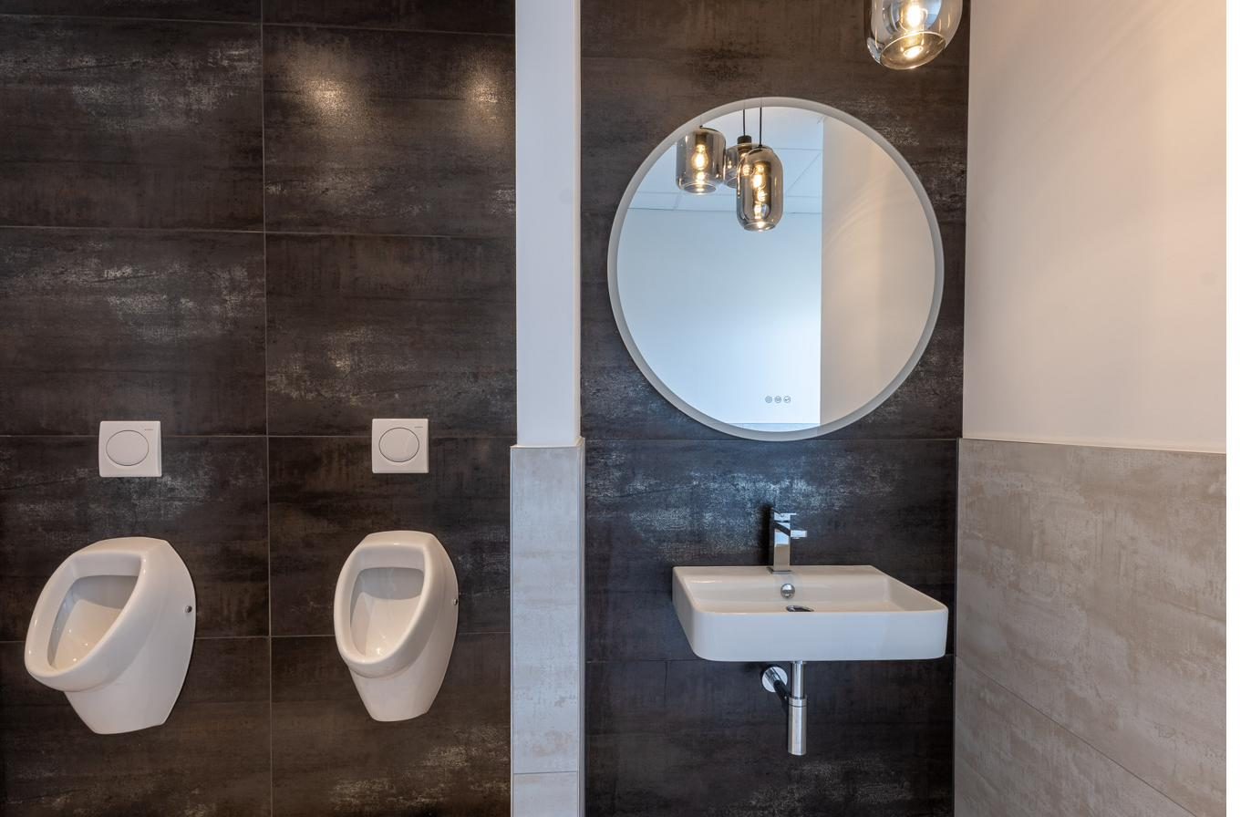 WC-Anlage mit dunklen Fliesen und Rundspiegel